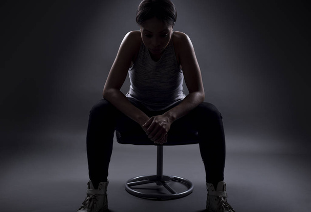 Silhouette di atleta donna nera seduta a riposare o prepararsi per una competizione o sconvolta per la perdita e il fallimento nello sport. La donna sembra grintosa su sfondo scuro
. - Foto, immagini