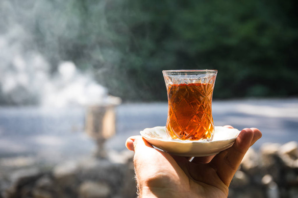 Восточный черный чай в стакане на руке женщины в лесу. Восточный чай. Традиционный кубок Армуду. Зеленый фон природы. Селективный фокус
 - Фото, изображение
