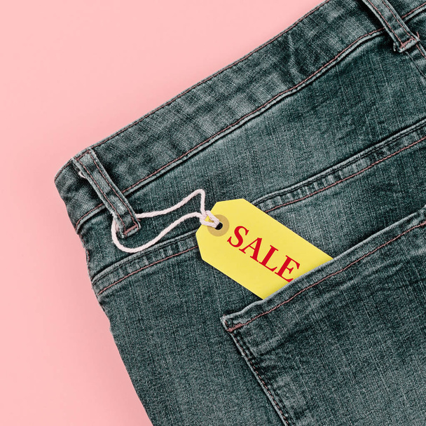Concept of sale black Friday and cyber Monday discounts tag with blue jeans on pastel pink background. Copy space, flat lay, square format - Foto, afbeelding