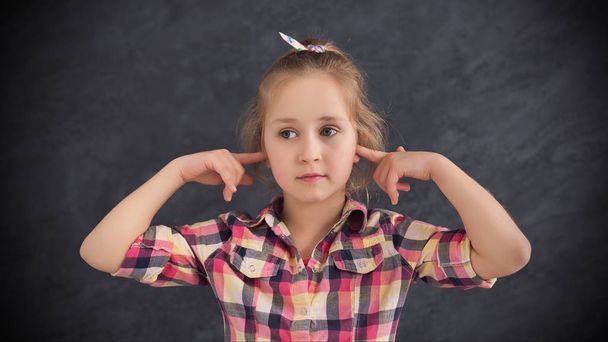 Κοριτσάκι κλειστά αυτιά με τα δάχτυλα σε γκρίζο φόντο - Φωτογραφία, εικόνα