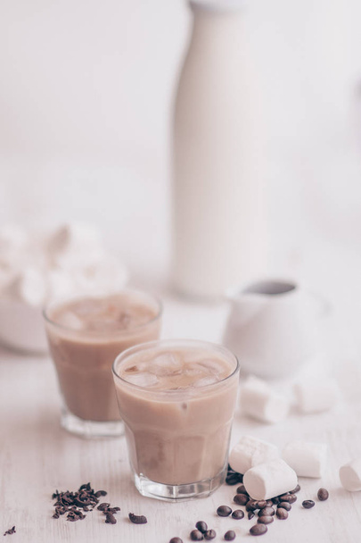 Light background. Iced coffee. Concept of a cooling drink. Marshmelow and coffee beans on the table. Summer drink. Cold coffee with milk and chocolate. - Photo, image