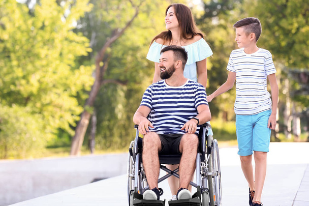Молодой человек в инвалидной коляске со своей семьей прогуливается на свежем воздухе
 - Фото, изображение