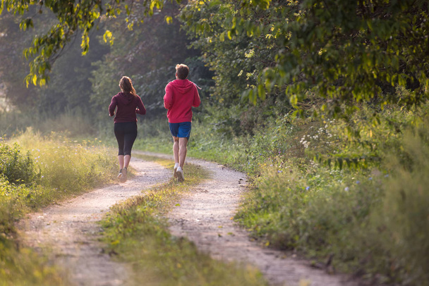 young couple enjoying healthy lifestyle while jogging along country road - Photo, image