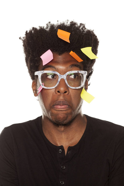 Vergeetachtig en verward jonge Afro-Amerikaanse man met stickers op zijn hoofd poseren op een witte achtergrond - Foto, afbeelding