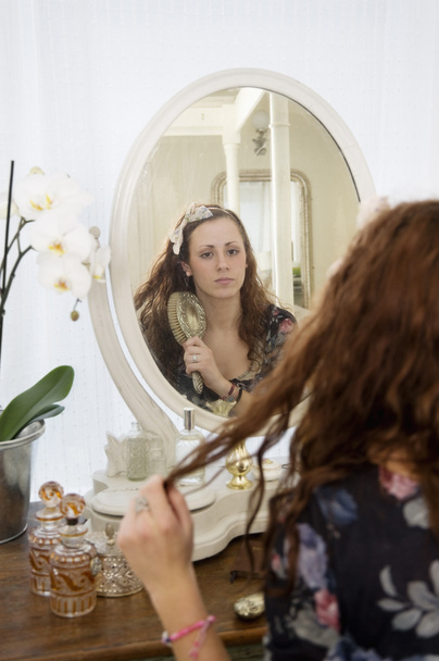 Young woman brushing her hair in front of mirror - Фото, изображение