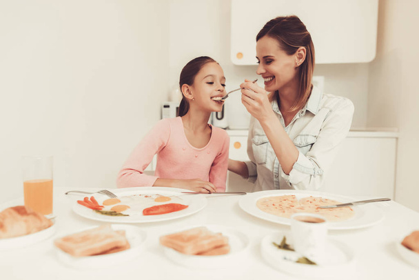 Mom With Daughter Are Having A Dinner At Kitchen. Family Relationship Concept. Having Fun During The Breakfast. Morning Nutricion. Chilling Together. Happy Childhood Concept. Time To Lunch. - 写真・画像
