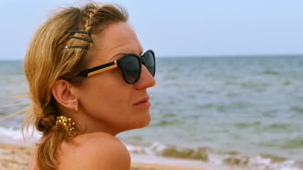 4 k. 女性座って海砂のビーチし、海の表面に見えます。顔をクローズ アップ - 映像、動画
