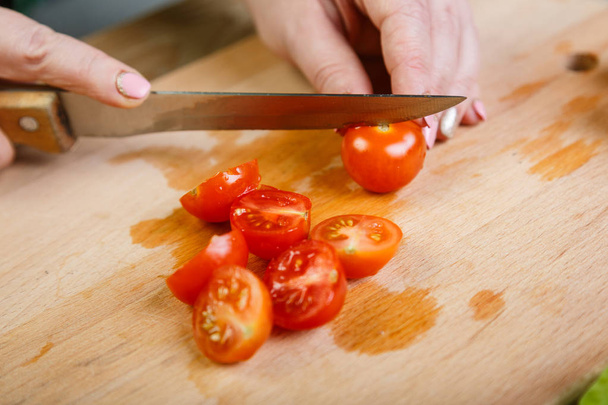 Na drewnianym stole kobieta tnie Pomidory czereśniowe dla Sałatka jarzynowa z nożem. Widok z przodu - Zdjęcie, obraz