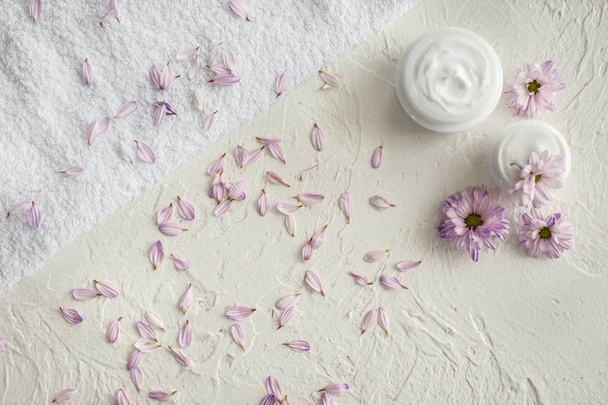 Frascos con crema corporal, pétalos de flores y toalla suave sobre mesa blanca
 - Foto, imagen