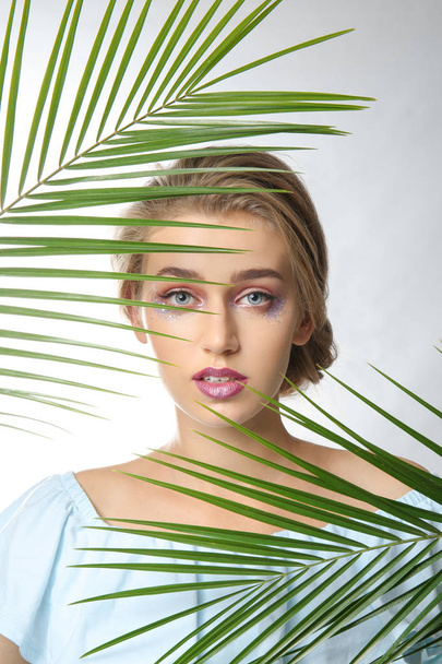 Young woman with beautiful makeup and tropical leaves on white background - Photo, Image