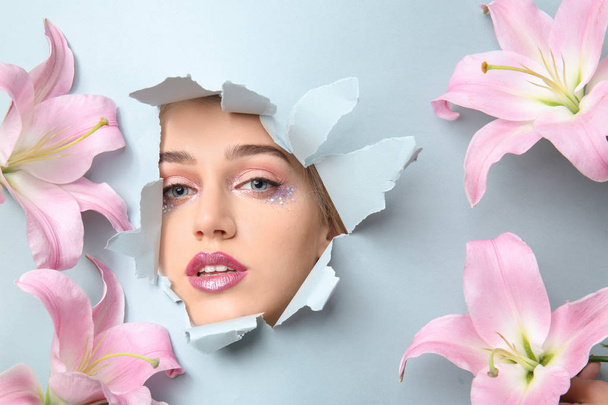 schöne Blumen und Gesicht der jungen Frau sichtbar durch ein Loch in zerrissenem Farbpapier - Foto, Bild