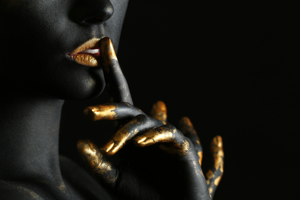 Όμορφη γυναίκα με το μαύρο και το χρυσό χρώμα στο σώμα της ενάντια σε σκούρο φόντο, κοντινό πλάνο - Φωτογραφία, εικόνα
