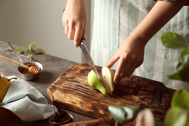 Woman cutting ripe pear for cake on wooden board - Photo, image