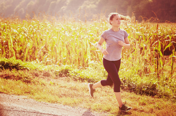 joven corredor femenino adulto disfrutando de un estilo de vida saludable mientras trota a lo largo del camino rural
 - Foto, imagen