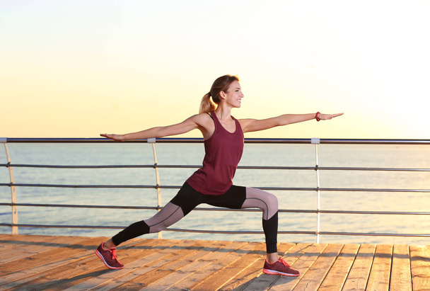 Young woman doing fitness exercises on pier in morning - Foto, immagini
