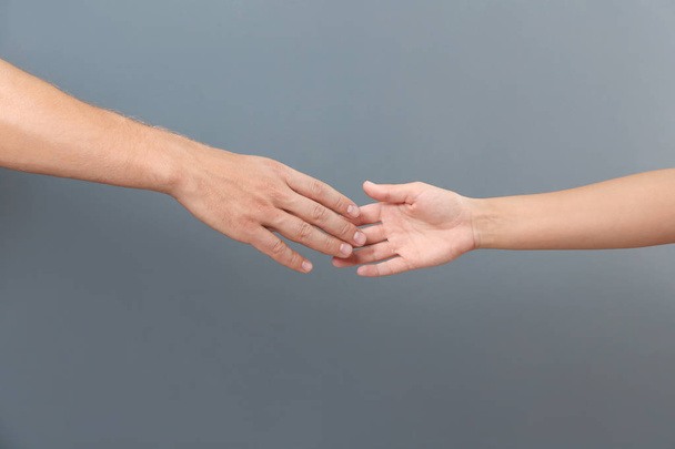 Mann und Frau reichen sich auf grauem Hintergrund die Hände. Konzept der Unterstützung und Hilfe - Foto, Bild