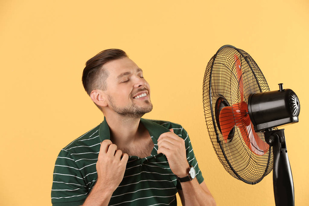 Man refreshing from heat in front of fan on color background - Фото, изображение