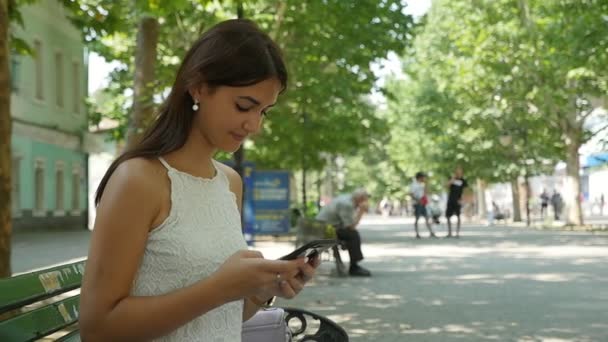 Attractive young woman seeking info on her phone in a street in summer in slo-mo                          Profile of a glamour young woman with long loose hair surfing the net on her smartphone outdoors on a sunny day in summer in slow motion - Felvétel, videó