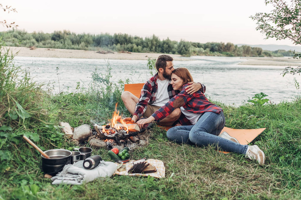 Happy Young Couple Sitting by Bonfire Having Picnic on Nature - Photo, Image