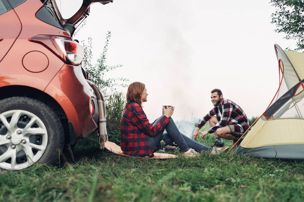 Happy Young Couple Sitting by Bonfire Having Picnic on Nature - Foto, imagen