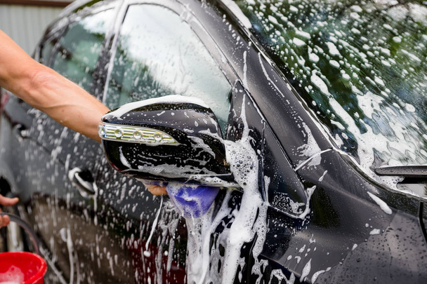 Cleaning automobile Using High Pressure Water. Man washing his car under high pressure water in service.worker washing car.Protection of car concept.male hand with purpl sponge washing auto.Selective - Fotografie, Obrázek