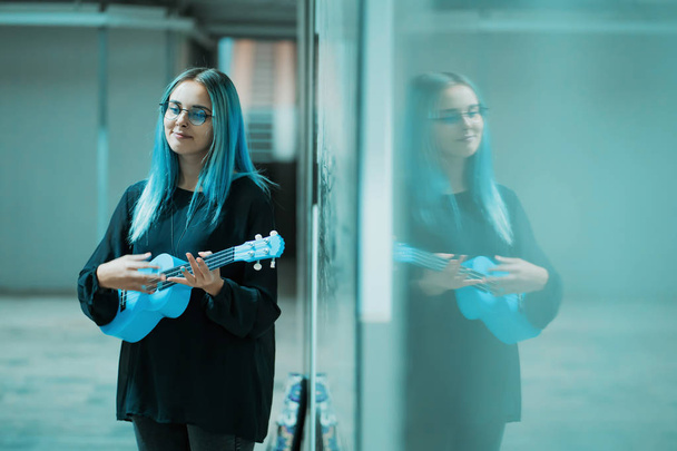 Joven chica bonita con el pelo azul jugando en ukelele azul en el paso subterráneo o metro
. - Foto, Imagen
