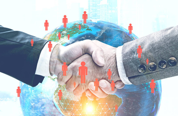 Silhouettes of two business leaders shaking hands in morning city. Glowing global world network hologram in the foreground. Toned image double exposure Elements of this image furnished by NASA - Photo, Image