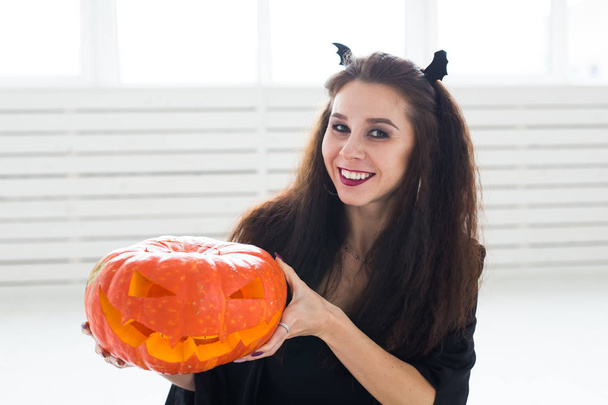 Hymyilevä brunette nainen halloween meikki poseeraa veistetty kurpitsa
 - Valokuva, kuva