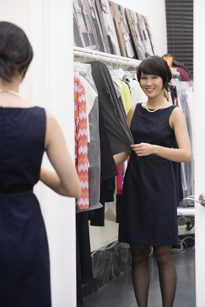 νεαρή γυναίκα να στέκεται από το ράφι ρούχα μπροστά από τον καθρέφτη - Φωτογραφία, εικόνα