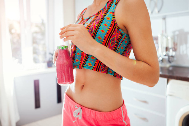 Woman drinking a homemade fruity detox smoothie wearing sportive clothing on kitchen. Healthy diet - Foto, Imagem