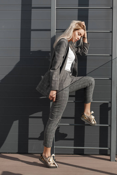 Linda jovem modelo de mulher elegante em moda vintage terno cinza posando perto da parede com uma escada rolante na rua
 - Foto, Imagem