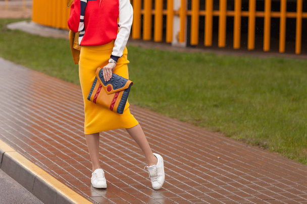 Ulicy, jasny styl. Młodą kobietę w spódnicy kurtka pomarańczowe, żółte, białe trampki, Okulary z torebka i mobile. Szczegóły. - Zdjęcie, obraz
