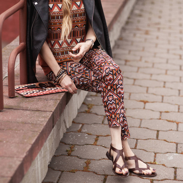 Straat, heldere stijl. Een jonge vrouw in het kostuum met ornament, zwarte jas, koppeling, sandalen, zonnebrillen. Details. Sguare afbeelding foto - Foto, afbeelding