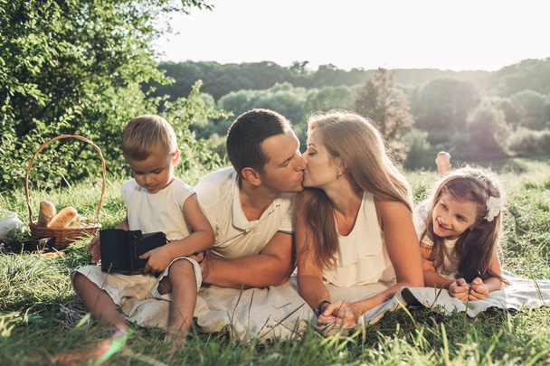Ενηλίκων ζευγάρι με τα παιδιά τους λίγο έχοντας πικ νικ το καλοκαίρι απολαμβάνοντας το πάρκο έξω από την πόλη, Σαββατοκύριακο έννοιας οικογένεια, τέσσερα άτομα - Φωτογραφία, εικόνα