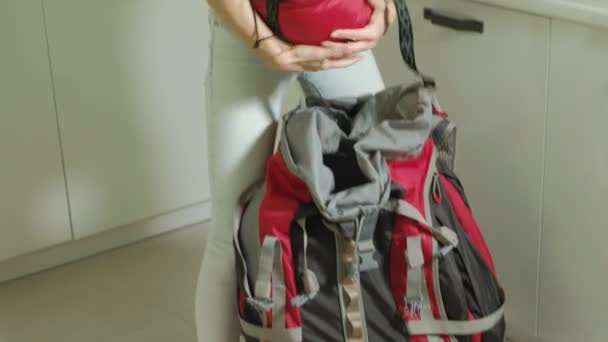 A woman tourist collects things in a backpack in the kitchen of the house and prepares for a trip - Séquence, vidéo