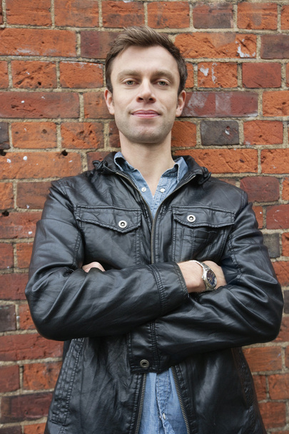 Portrait of man in leather jacket standing against brick wall - Фото, изображение