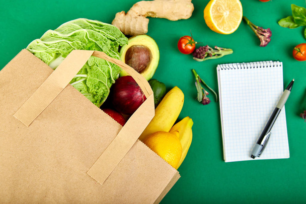 Shopping list, recipe book, diet plan. Grocering concept. Full paper bag of different fruits and vegetables,  ingredients for healthy cooking on a color background. healthy food.  Diet or vegan food, vegetarian. Top view. Flat lay.  - Photo, Image
