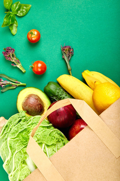  Grocering concept. Full paper bag of different fruits and vegetables,  ingredients for healthy cooking on a color background. healthy food.  Diet or vegan food, vegetarian. Top view. Flat lay.  - Photo, Image