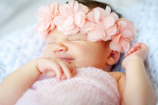 Leuk en schattig Kaukasische pasgeboren babymeisje met een roze bloem-head band glimlachend in haar slaap. - Foto, afbeelding