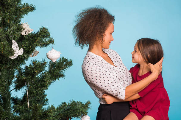 Μικτή φυλή μαμά και την κόρη με το χριστουγεννιάτικο δέντρο σε μπλε φόντο - Φωτογραφία, εικόνα