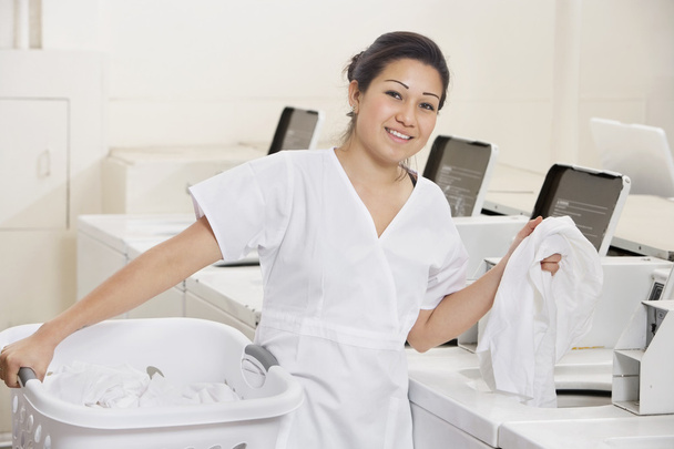 Portrait of a happy young employee putting clothes in washing machine - Photo, Image