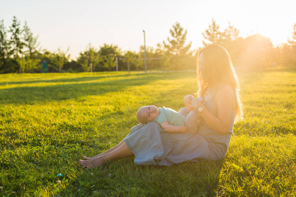 Young woman with boy on the meadow on a sunny day. Happy family on summer sunset. Mother with baby. - Фото, изображение