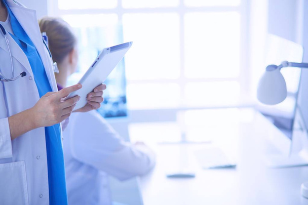 Nahaufnahme von Ärzten, die Tablette in der Hand halten, und Kollegen, die im Hintergrund am Tisch sitzen - Foto, Bild