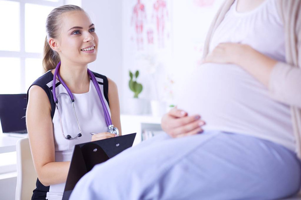Fiatal nő orvos sztetoszkóppal és tablettával beszél terhes nővel a kórházban. - Fotó, kép