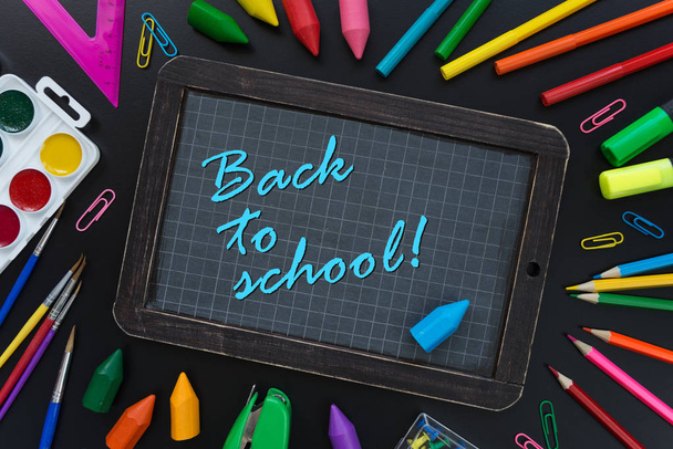 Back to school background with checkered chalkboard surrounded by multicolored school supplies are on black background - Фото, зображення