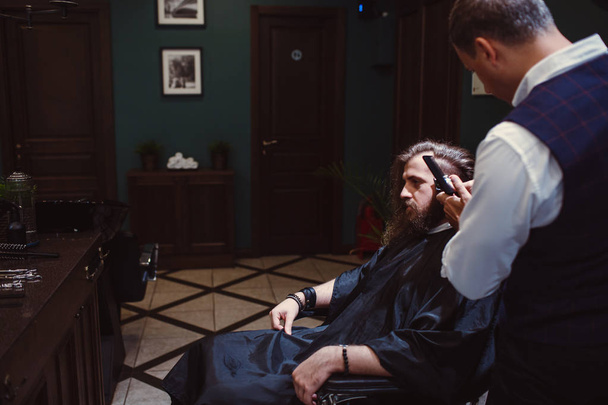 Barbershop with wooden interior. Bearded model man and barber. - Photo, Image