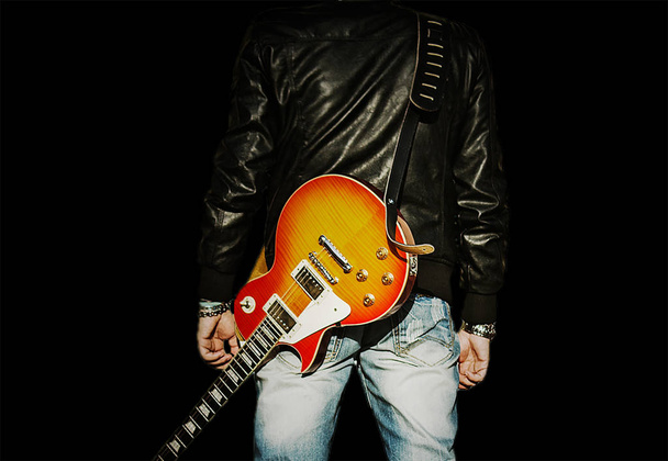 Achteraanzicht van een man met een gitaar op zijn schouder geïsoleerd op zwarte achtergrond - Foto, afbeelding