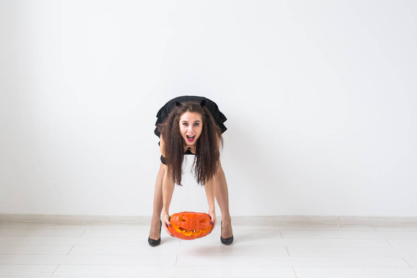 Halloween en maskerade concept - mooie jonge vrouw poseren met pompoen Jack-o-lantaarn op lichte achtergrond met kopie ruimte - Foto, afbeelding