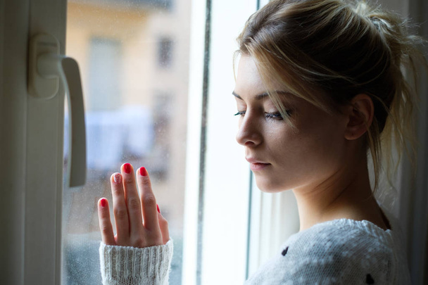 Красивая грустная девушка у окна в холодный день
 - Фото, изображение