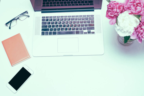 Workplace with laptop, glasses, notebook and pink and white peony flowers on the white table background. Flat lay, top view - Foto, Imagem